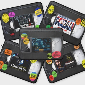 Może przedstawiać: Sześć czarnych futerałów na laptopa w stylu kasety VHS z różnymi tytułami i obrazami filmów grozy. Futerały zawierają tytuły takie jak "Piątek 13", "Krzyk", "Halloween", "Zabójcza zabawka" i "Koszmar z ulicy Wiązów".