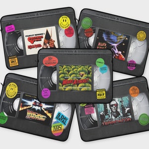 Puede incluir: Seis fundas para portátil negras con forma de cinta VHS con etiquetas y títulos coloridos. Los títulos incluyen "Stanley Kubrick's The Shining", "Mars Attacks", "Regreso al futuro", "Killer Klowns from Outer Space", "Terminator" y "Alquiler de 7 días".