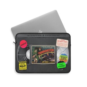 Retro Horror VHS Laptop Sleeve available in three sizes to protect your laptop. Printed on one side with a black backside, edging and zip, the perfect addition to your movie monsters, 80s, 90s, VHS tape Frankenstein, Dracula, themed desk or computer.