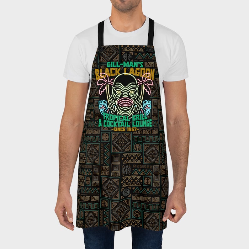 Our Gill Mans Black Lagoon Tropical Grill & Cocktail Lounge Apron is the perfect kitchen cooking accessory gift for any vintage horror movie fan that loves Creature from the Black Lagoon, Universal Monsters, and baking or cooking.