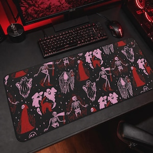 May include: Black rectangular mouse mat with a Halloween design. The pattern features pink ghosts, red-robed figures, skeletons, and black cats on a black background. The mat is designed for a computer setup.