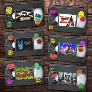 Può includere: Set di 8 sottobicchieri neri in stile VHS con titoli di film e adesivi. I sottobicchieri presentano titoli come "Ritorno al futuro", "Donnie Darko", "Mars Attacks!" e "Terminator 2".