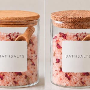 May include: Two clear glass jars filled with pink bath salts and dried rose petals. Each jar features a white square label with the text BATHSALTS, a small wooden scoop inside, and a round lid, one made of smooth wood and one of textured cork.