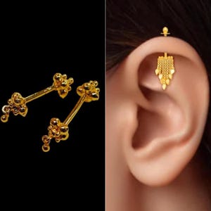 May include: A pair of gold ear cartilage barbell earrings with a cluster of small balls on each end. The earrings are shown on a model's ear with a dangling gold charm.