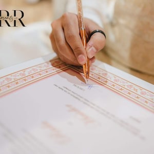 May include: A person signing a document with a rose gold pen. The document has a pink and gold border with a floral pattern. The text "moments..." is visible in the top left corner of the image.