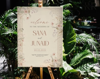 May include: A wedding welcome sign with a floral design and the text "welcome to the wedding of Sana and Junaid 10.12.2021" and the quote "And We created you in pairs".