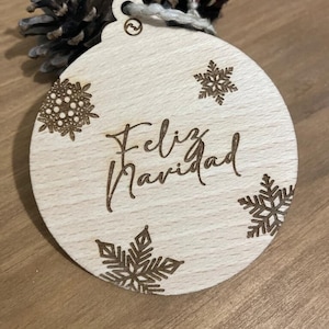 Op de afbeelding: Een houten kerstversiering met de tekst "Feliz Navidad" en sneeuwvlokontwerpen.