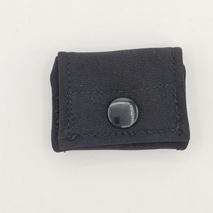 Könnte beinhalten: Eine kleine schwarze Tasche mit einem einzigen schwarzen Knopf. Der Knopf hat einen silbernen Rand.