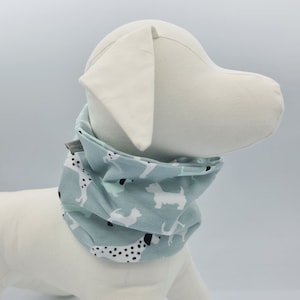 Könnte beinhalten: Ein hellblaues Hundehalstuch mit weißem Hintergrund und einem Muster aus schwarzen und weißen Hunden. Das Halstuch ist aufgerollt und um eine weiße Hunde-Puppe gebunden.