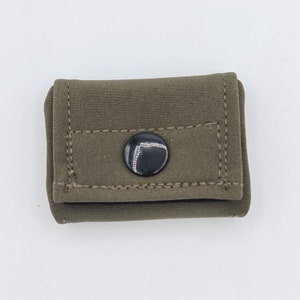 Könnte beinhalten: Olivgrüne Stofftasche mit schwarzem Knopfverschluss. Die rechteckige Tasche ist gefaltet, mit sichtbaren Nähten an den Kanten. Der Knopf ist mittig angebracht und bietet einen sicheren Verschluss für kleine Gegenstände.