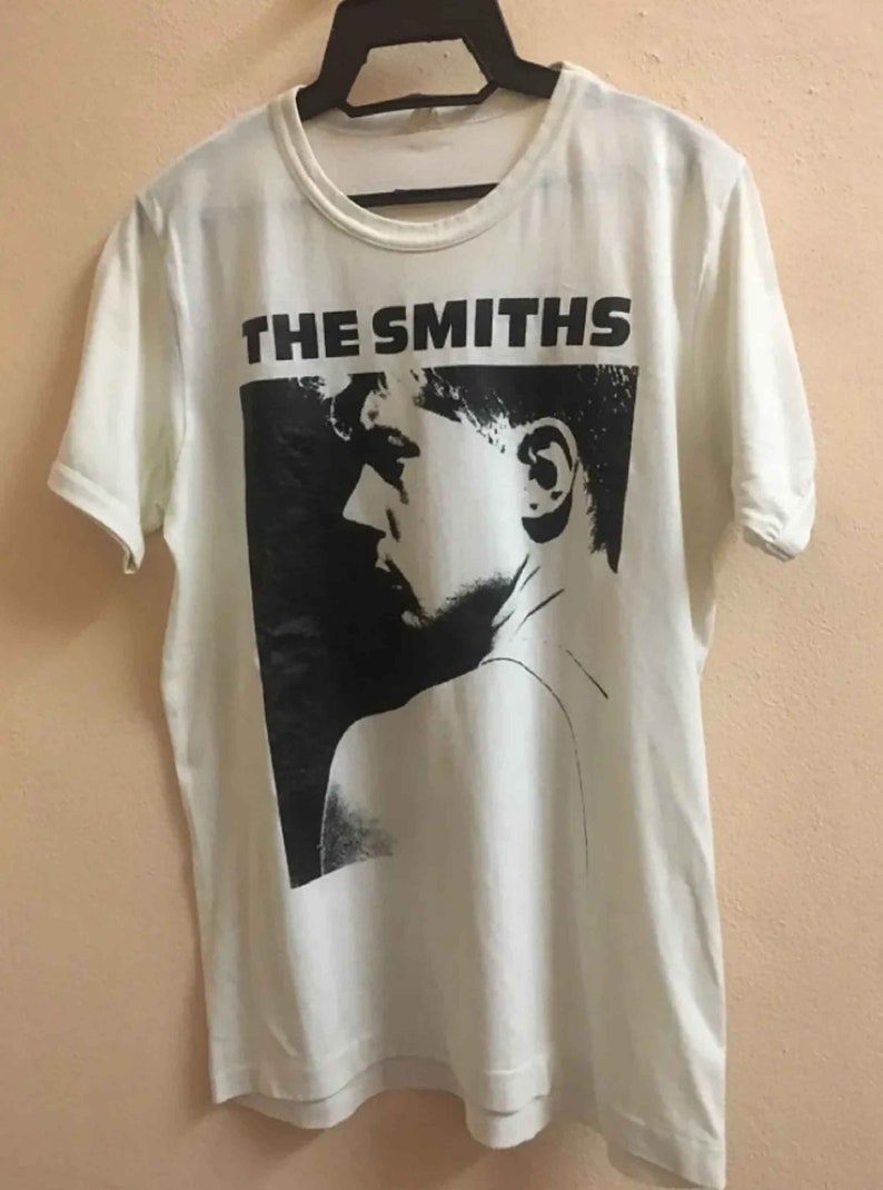 Puede incluir: Camiseta blanca con una imagen en blanco y negro de la cara de una persona y el texto "THE SMITHS" impreso en la parte delantera.