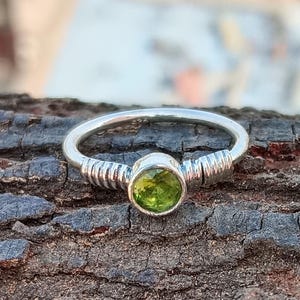 May include: A silver ring with a green gemstone set in a bezel setting. The ring has a textured band.