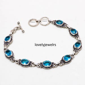 May include: A silver bracelet featuring oval-shaped, bright blue gemstones. The gemstones are set in ornate, detailed silver settings and connected by a delicate chain. The bracelet has a toggle clasp. The text "lovelyjewelrs" is visible.