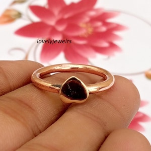 Peut inclure: Une bague couleur or rose avec un petit cœur lisse en son centre. L'anneau est circulaire et poli, avec le texte lovelyjewelrs visible en arrière-plan. Le métal présente un éclat métallique chaud sur l'ensemble de la pièce.
