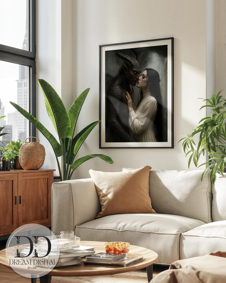 May include: A framed wall art print featuring a dark, moody illustration of a horned, dark-skinned figure embracing a person with long dark hair in a white dress. The artwork is displayed in a thin black frame, showcasing a romantic, gothic scene.