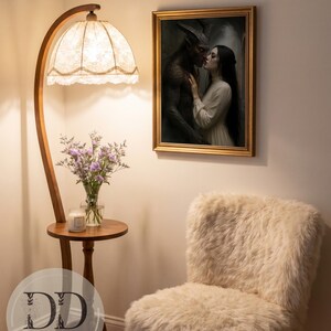 May include: A framed wall art print depicting a dark horned figure and a person in a cream dress, positioned near a wooden floor lamp with a lace shade, a small round table holding a glass vase of purple flowers, and a cream-colored faux fur chair.