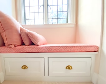 May include: A white window seat with two drawers and a pink cushion. The cushion has a chevron pattern and is topped with two pink pillows.