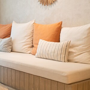 wooden bench with a pillows and beige bench cushion. The pillows are white, orange, and striped.