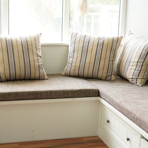 May include: A white window seat with a brown linen L shape bench cushion and three striped pillows.