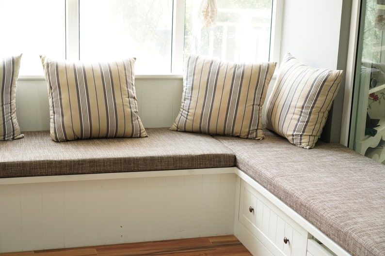 May include: A white window seat with a brown linen L shape bench cushion and three striped pillows.
