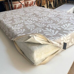 A beige cushion with a white leaf boho pattern. The cushion is zippered and has a removable, white foam insert.