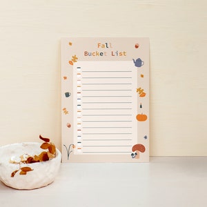 May include: A printable fall bucket list with a beige background and colorful illustrations of leaves, a teapot, a pumpkin, and a mushroom. The text "Fall Bucket List" is printed in black at the top of the page.