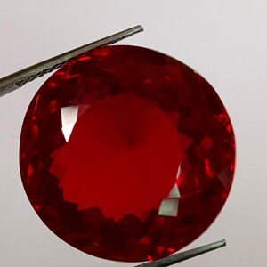Peut inclure: Une pierre précieuse rouge foncé, ronde et facettée est maintenue par une pince. Les facettes réfléchissent la lumière, créant des reflets brillants. La pince est de couleur métal foncé, et le fond est blanc uni.