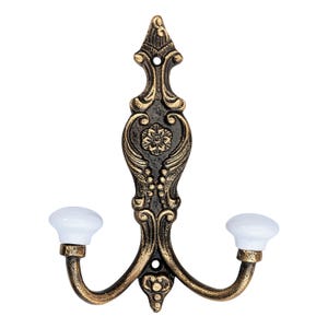 May include: Ornate, antique-style wall hook with a bronze finish and two curved arms. The hook features a decorative floral design and white ceramic knobs. Ideal for hanging coats, hats, or other items.