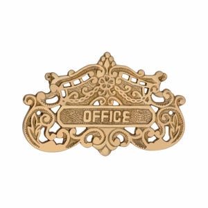 May include: Ornate gold-colored metal sign with the word "OFFICE" in a rectangular panel. The sign features intricate scrollwork and decorative flourishes, suitable for an office door or wall.