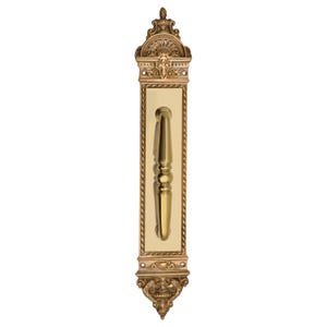 May include: Ornate brass door pull with a decorative design. The pull features a long, rectangular backplate with a central handle and intricate detailing at the top and bottom. The handle is a light gold color.
