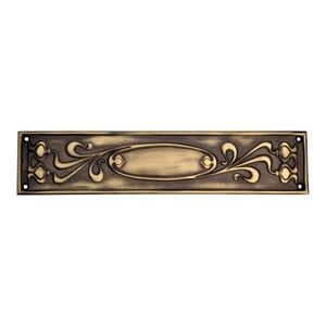 May include: An antique brass door plate, rectangular with an oval central panel and floral scrollwork. The plate has a dark, aged finish and four screw holes, showcasing an Art Nouveau design, typical of the era.