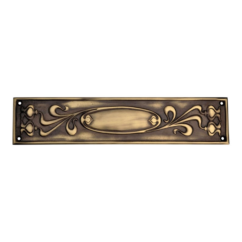 May include: An antique brass door plate, rectangular with an oval central panel and floral scrollwork. The plate has a dark, aged finish and four screw holes, showcasing an Art Nouveau design, typical of the era.