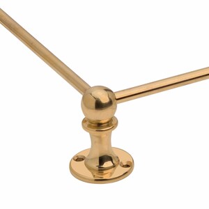 May include: A close-up of a brass-colored, decorative metal fixture. The fixture has a circular base with three screw holes, a central stem, and a spherical top where three rods meet. The rods extend outward at 90-degree angles.