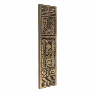 May include: A rectangular, bronze-colored decorative door plate with intricate floral and geometric carvings. The design includes flowers, a sunburst, and a vase with a plant. The plate has pre-drilled holes for mounting.