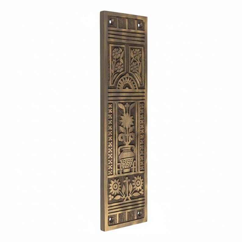 May include: A rectangular, bronze-colored decorative door plate with intricate floral and geometric carvings. The design includes flowers, a sunburst, and a vase with a plant. The plate has pre-drilled holes for mounting.