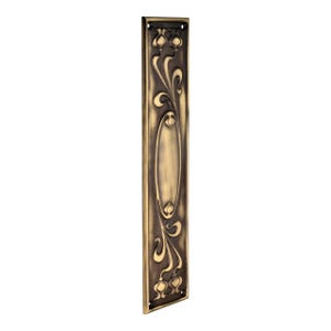 May include: A bronze-coloured door plate with an Art Nouveau design. The rectangular plate features an oval centre and floral and vine motifs. The plate has a dark, aged finish and is likely made of metal. Includes small holes for mounting.