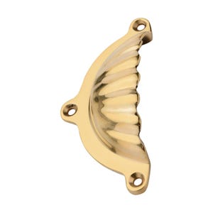 Puede incluir: Un tirador de armario pulido en forma de concha de lat&oacute;n con un dise&ntilde;o acanalado. El tirador tiene tres orificios de montaje y una forma curva, adecuado para cajones o puertas de armarios. El herraje es de color dorado c&aacute;lido.