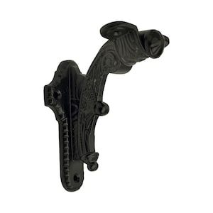 Puede incluir: Gancho de pared negro y ornamentado con un diseño decorativo en forma de voluta. El gancho presenta un brazo curvado y una placa de montaje con un patrón detallado. El gancho de metal está diseñado para montarse en una pared.