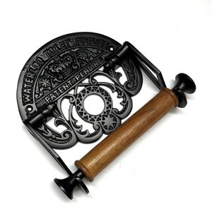 May include: Black cast iron toilet paper holder with a wooden roller and the text "Waterloo Toilet Fixture Patent Pending" on the front.