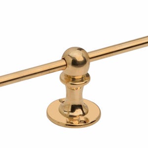 May include: A gold-colored towel bar with a round base and a decorative ball detail. The bar is straight and horizontal, with a polished finish. The fixture is designed for mounting on a wall.