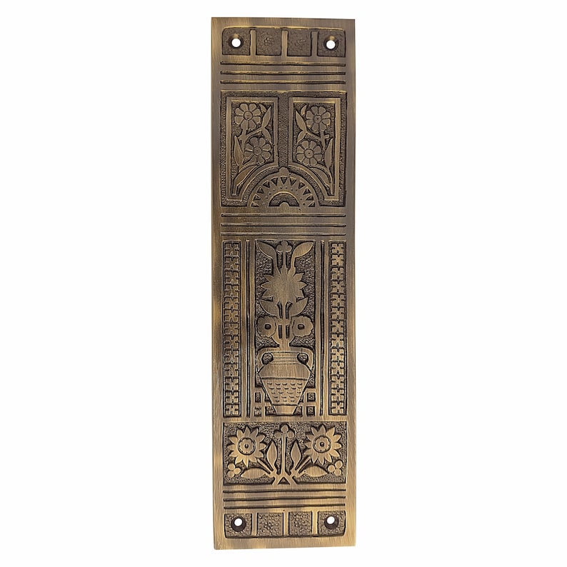 May include: A rectangular, antique brass door plate with intricate floral and geometric relief carvings. The design includes stylized flowers, a vase with foliage, and decorative borders. The plate has pre-drilled holes for mounting.