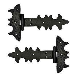 Può includere: Due cerniere in ferro battuto nero. Ogni cerniera presenta un design decorativo ad ala di pipistrello e una serie di bordi appuntiti. Le cerniere sono collegate da un perno centrale e hanno più fori per le viti.