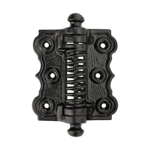 May include: A black spring hinge with decorative edges and a central spring mechanism. The hinge has a textured finish and features multiple screw holes for mounting. The design includes a rounded top and bottom.
