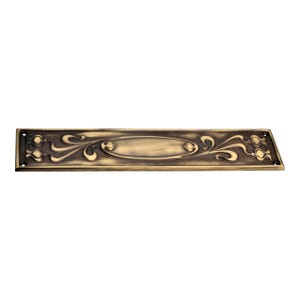 May include: An antique brass-coloured metal plate with an Art Nouveau design. The rectangular plate features an oval centre and stylized floral and swirling patterns. It has four screw holes at each end.