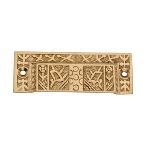 May include: A rectangular brass drawer pull with an intricate floral and geometric design. The pull features two circular holes for mounting and a recessed handle area with detailed carvings of flowers, leaves, and circles. The overall color is a warm, antique gold.