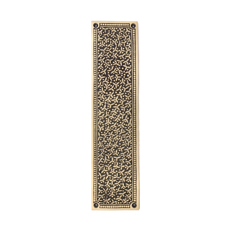 May include: A rectangular, brass-colored door pull with an intricate, repeating floral pattern. The edges are lined with small, evenly spaced dots. The design is centered on a dark background, creating a contrast. The door pull has a vintage aesthetic.
