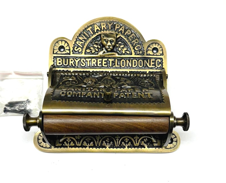 May include: Antique brass toilet roll holder with a wooden roller and ornate detailing. The holder features the text "SANITARY PAPER BURY STREET LONDON EC COMPANY PATENT".