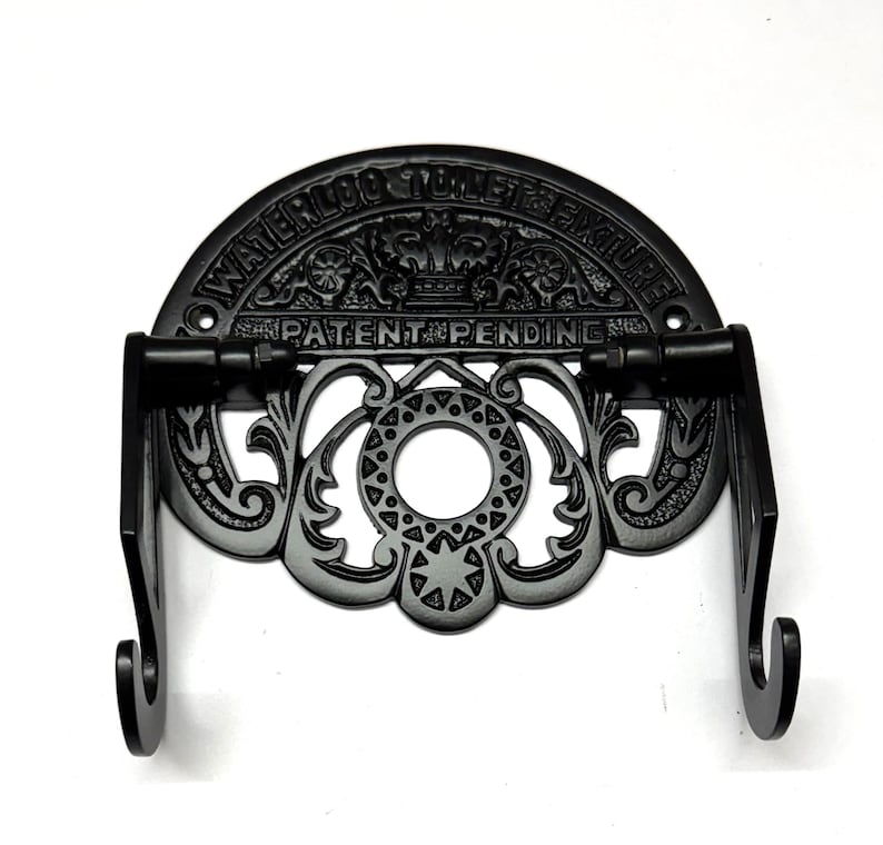 May include: Black cast iron toilet paper holder with a decorative design and the text "Waterloo Toilet Fixture Patent Pending".