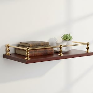 Puede incluir: Una estantería de madera marrón oscuro con detalles de latón. Exhibe libros antiguos, una pequeña planta suculenta en maceta y un juego de tazas. La barandilla de latón añade un toque decorativo.