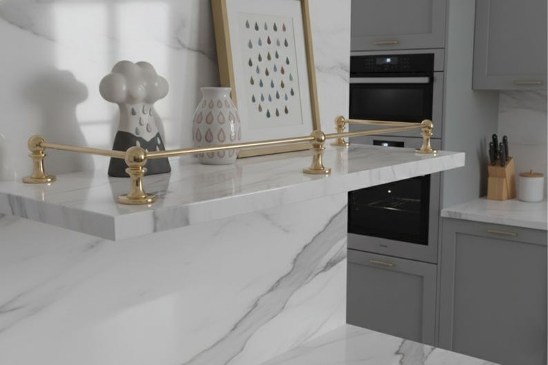 May include: A modern kitchen shelf with a gold-colored railing. The shelf is made of white marble and features decorative items, including a cloud-shaped sculpture and a vase. A framed picture with a teardrop design is also on the shelf.